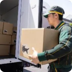 緑の制服を着た配達員が、積まれた荷物から一つを持ち出す様子。