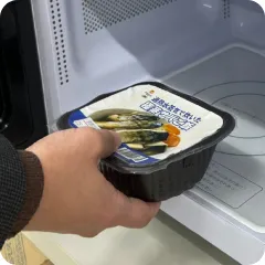 温かい夕食の準備：電子レンジにパック食品を入れる手元。